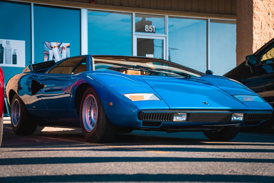 A stunning blue luxury sports car parked outside a modern building on a sunny day.