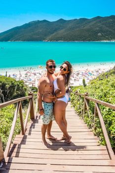 Couple posing joyfully on wooden stairs overlooking a sunny beach.