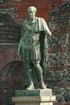 Ancient Roman statue in traditional attire with brick wall in the background.