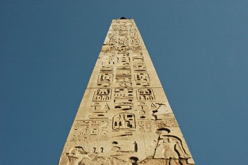 Free View of an ancient Egyptian obelisk with hieroglyphic carvings against a clear blue sky. Stock Photo