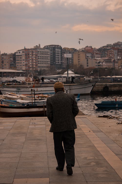 A Back View of a Man Walking on a Concrete Dock Towards the Boats