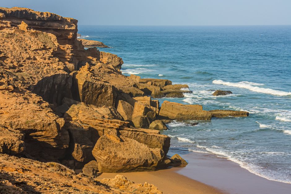 Breathtaking view of coastal cliffs with waves crashing against the rocks under the bright day sky.