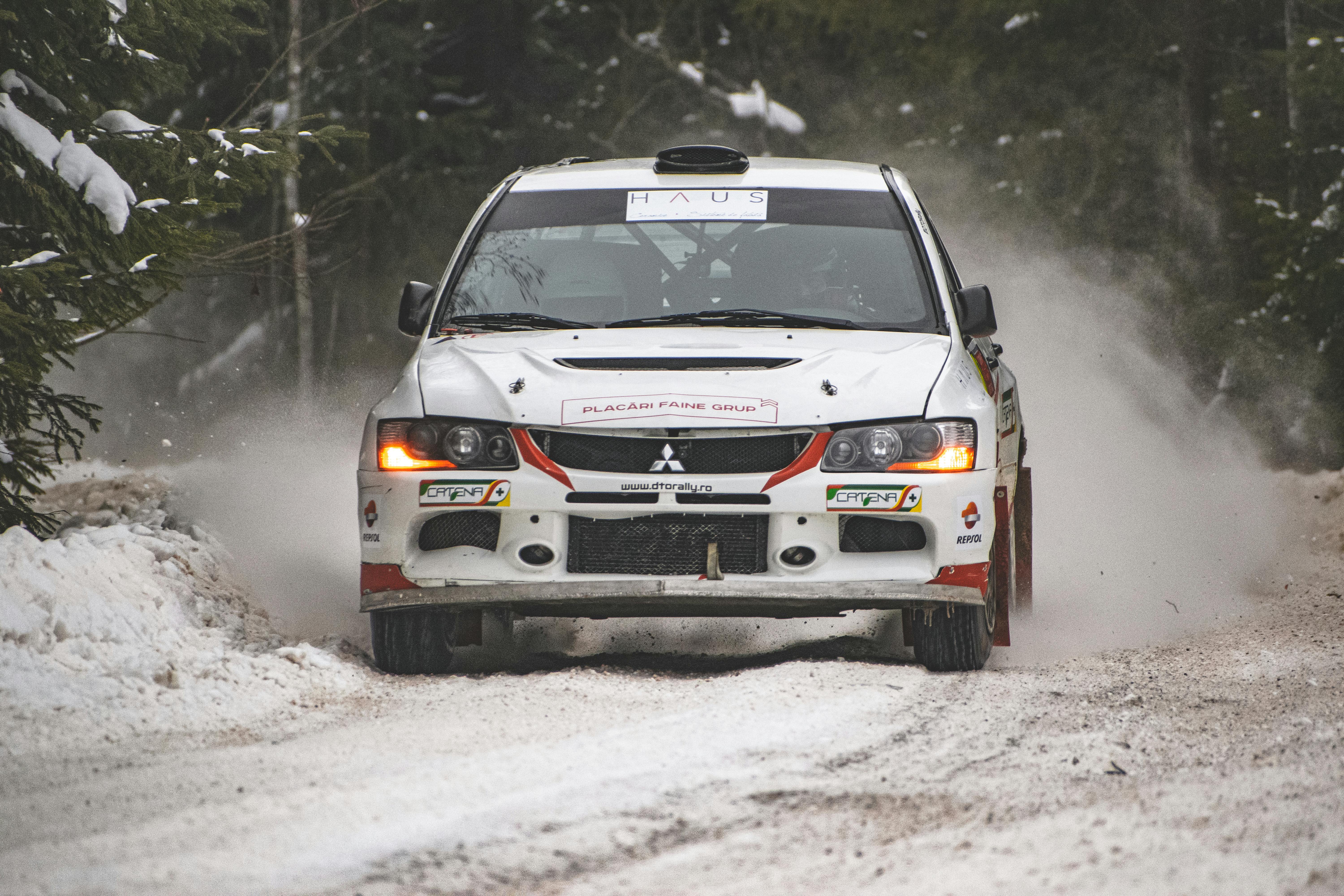 Dynamic shot of a Mitsubishi Lancer Evolution racing through snowy Romanian forests during a winter rally.