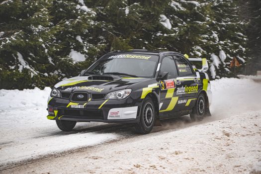 A rally car speeds through snowy roads in a winter race, showcasing skill and precision.