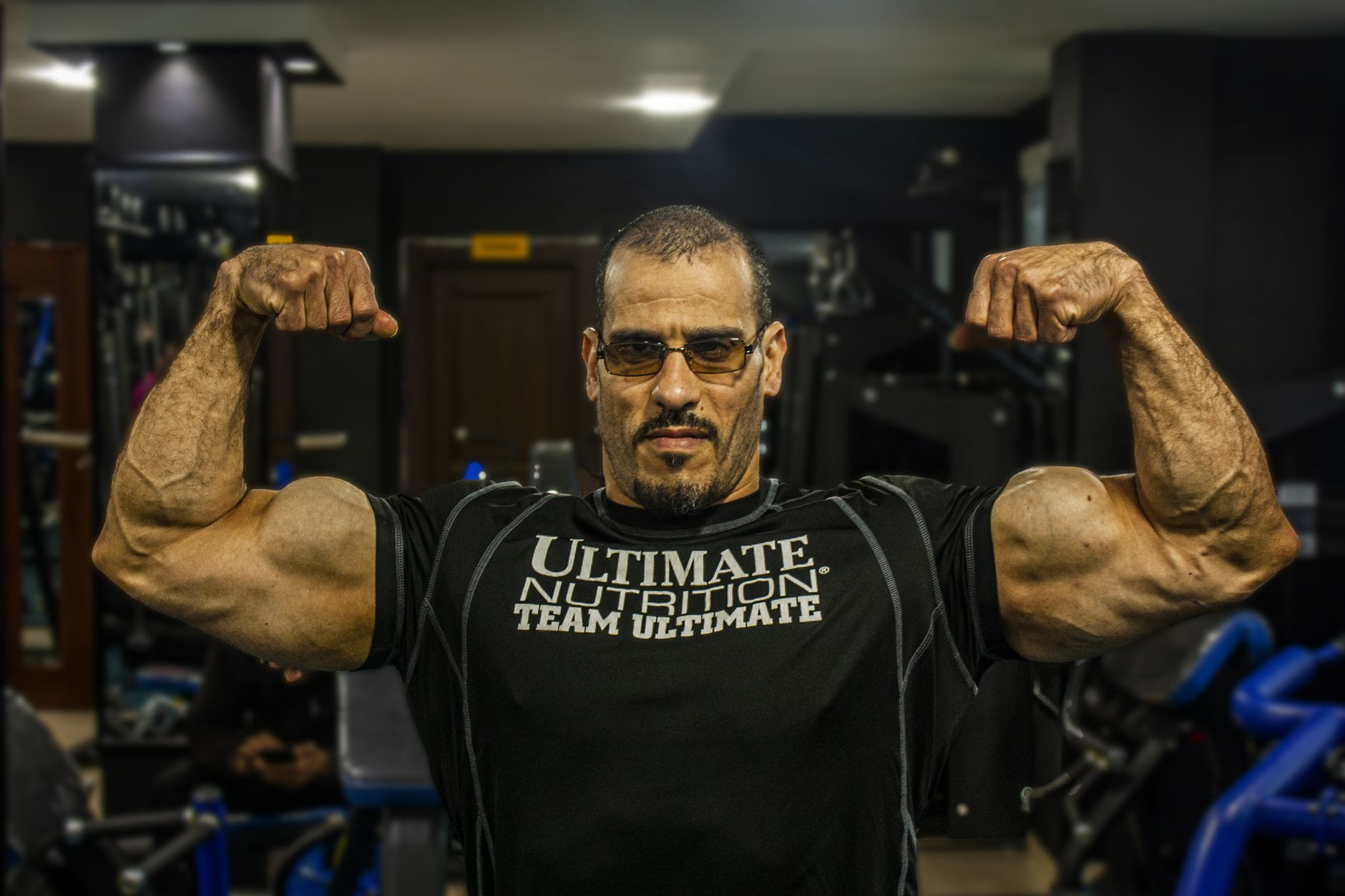 Strong man flexing biceps at gym showcasing bodybuilding physique.
