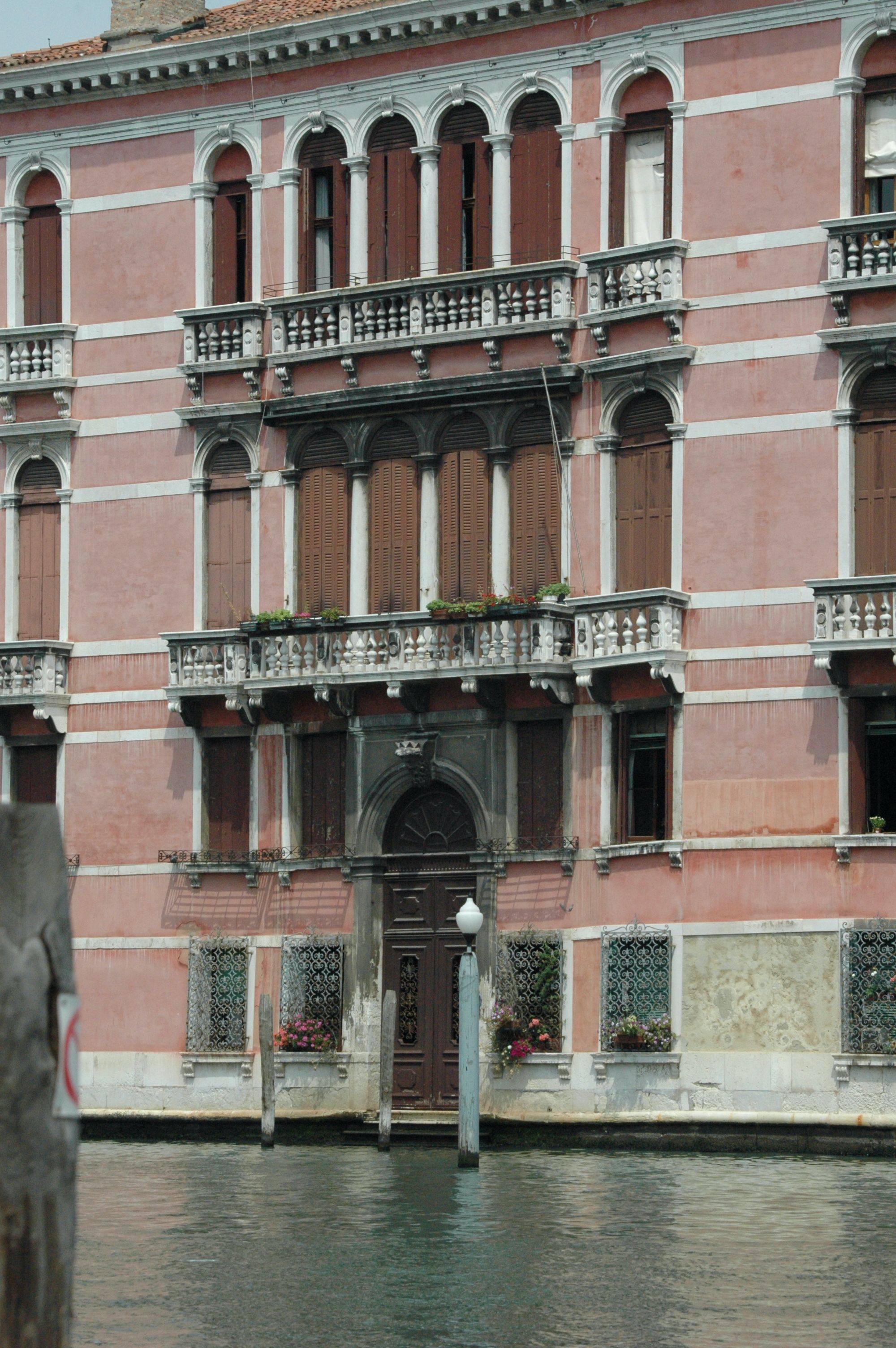 Charming pink façade of historic Venetian building beside a serene canal, showcasing classic architecture.