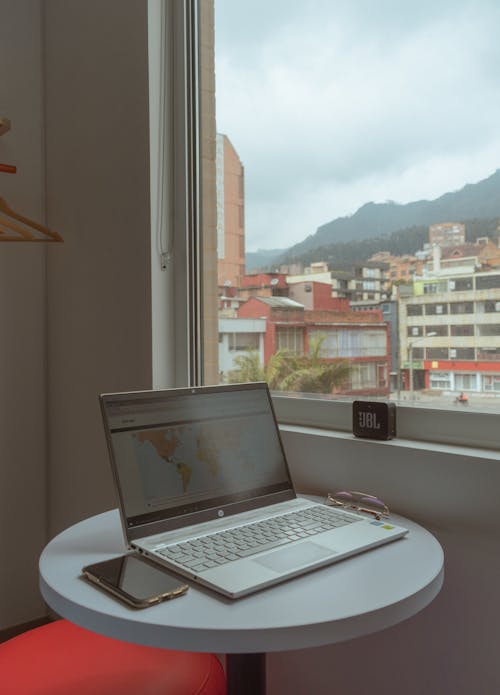 A Laptop and Mobile Phone on the Table Near the Window with a City View