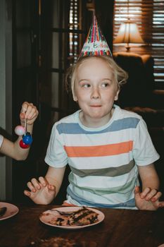 A child enjoying a birthday party indoors with a colorful party hat and cake.