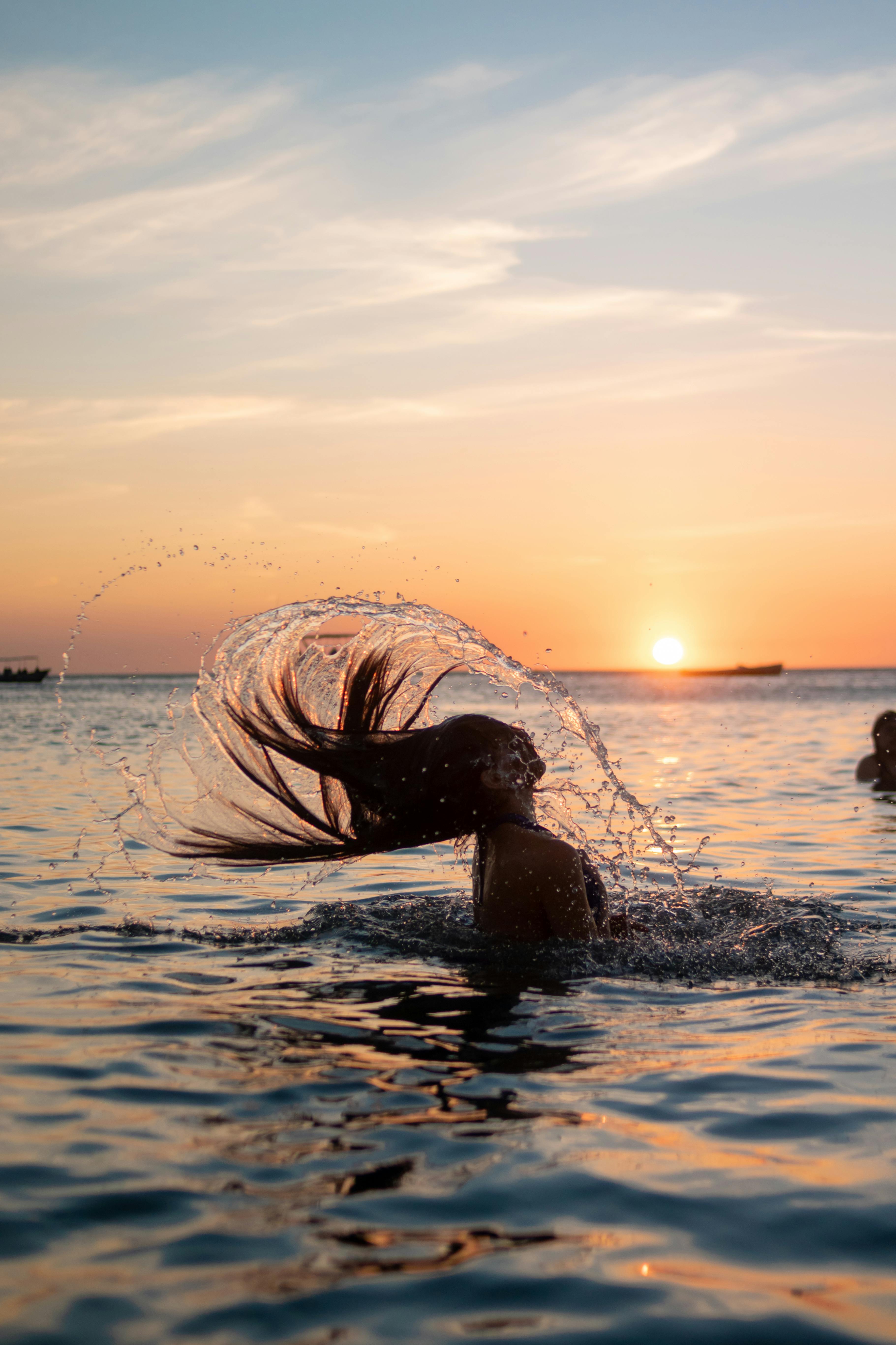 A woman performs a hair flip in the ocean during sunset at Santa Marta beach.