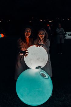 两名女子在夜晚的户外享受着发光球体，欢乐的氛围被捕捉下来