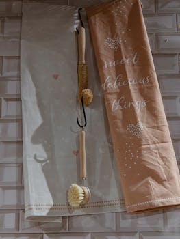Two kitchen towels and wooden brushes on tiled wall, featuring "sweet delicious things" text.
