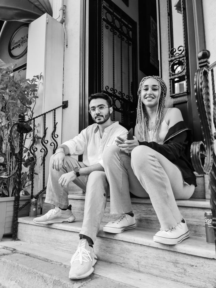 A Grayscale Photo Of A Man And Woman Sitting On The Steps Near The Front Door