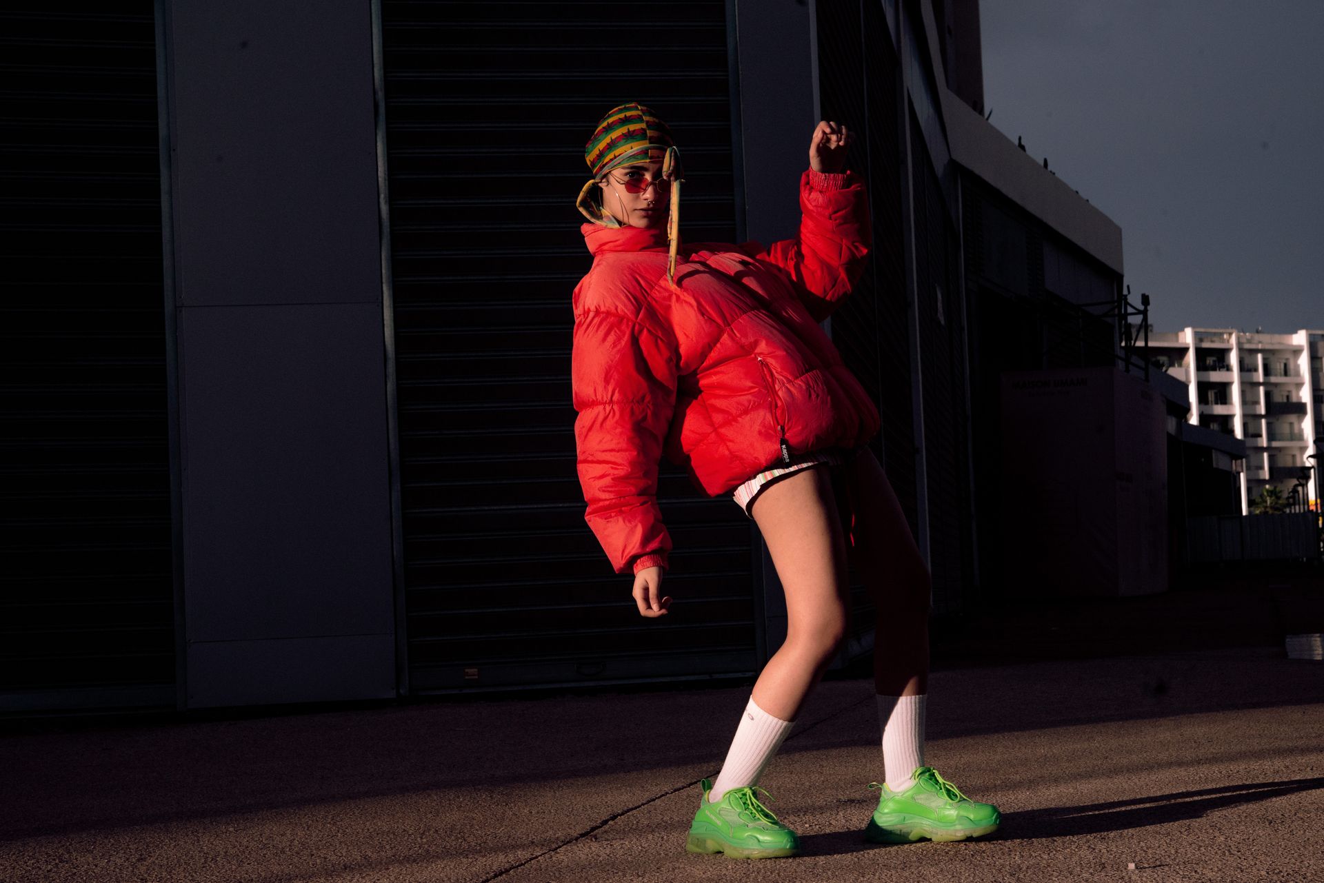 Stylish woman posing in urban setting wearing a red jacket, white socks, and green shoes.