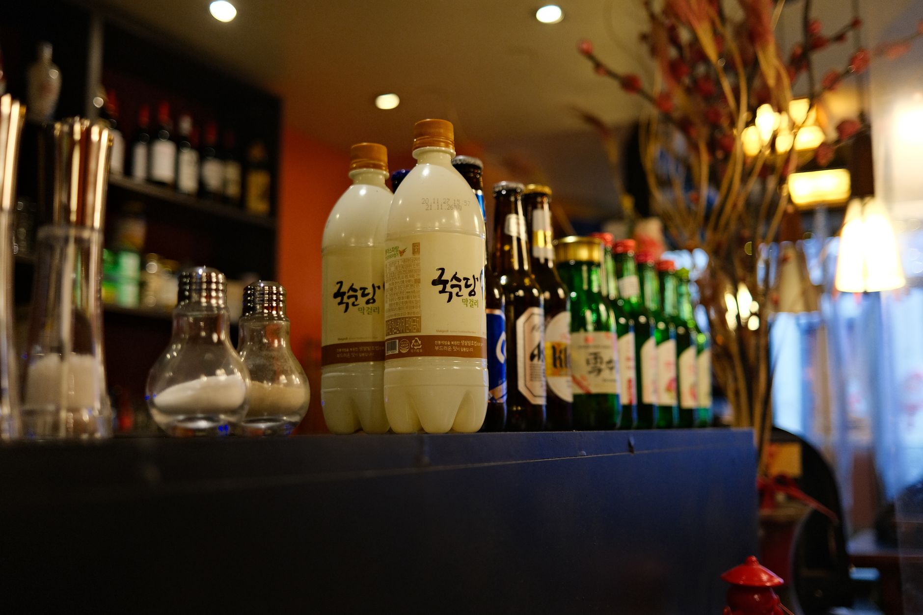 Display of assorted liquor bottles and seasoning shakers on a black table in ambient bar setting.