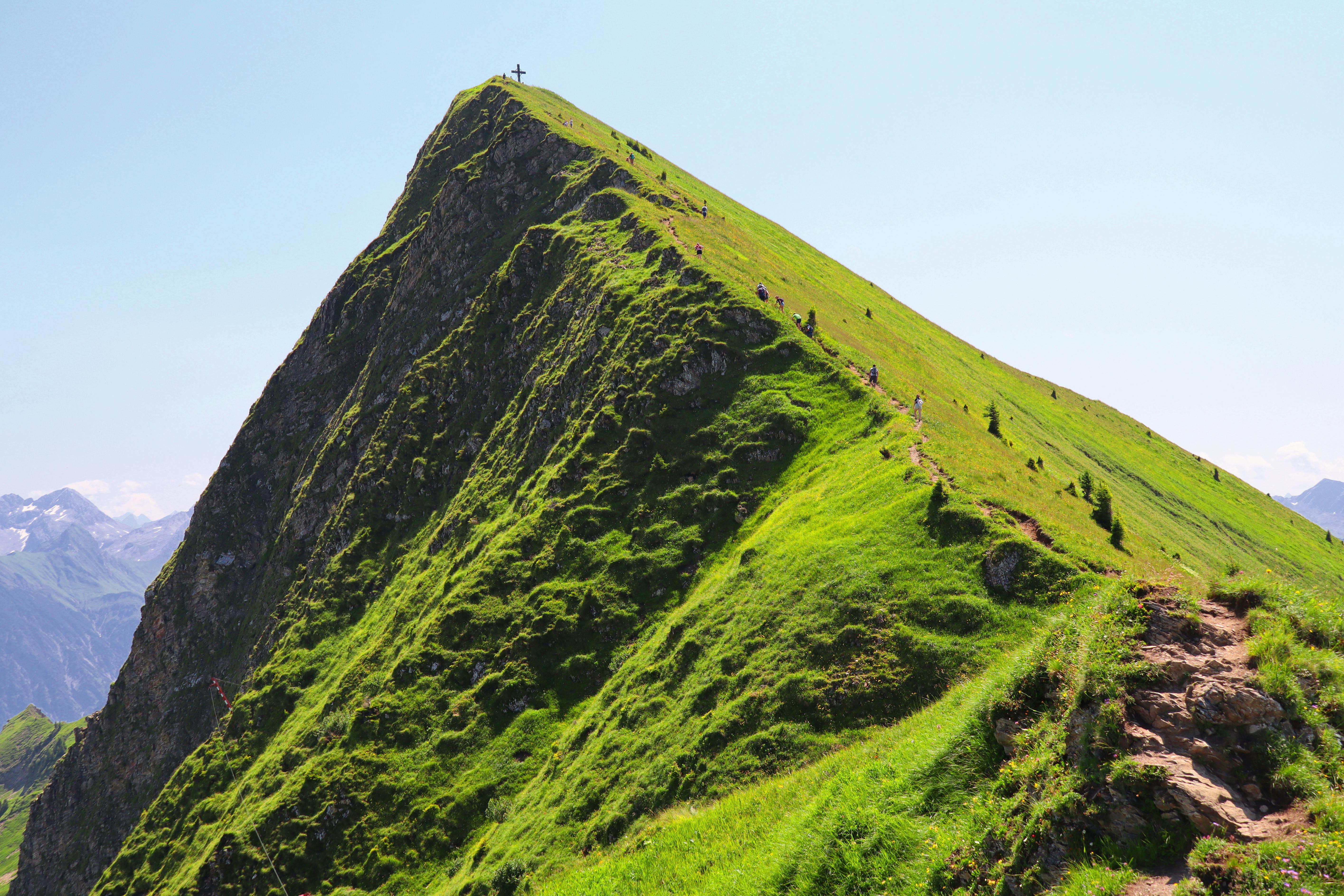 Green mountain peak with hikers on a sunny day, perfect for nature lovers.