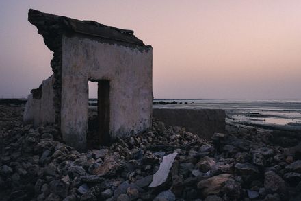 Weathered stone ruin on a rocky shoreline at dusk — photo by Pareekshith Indeever on Pexels