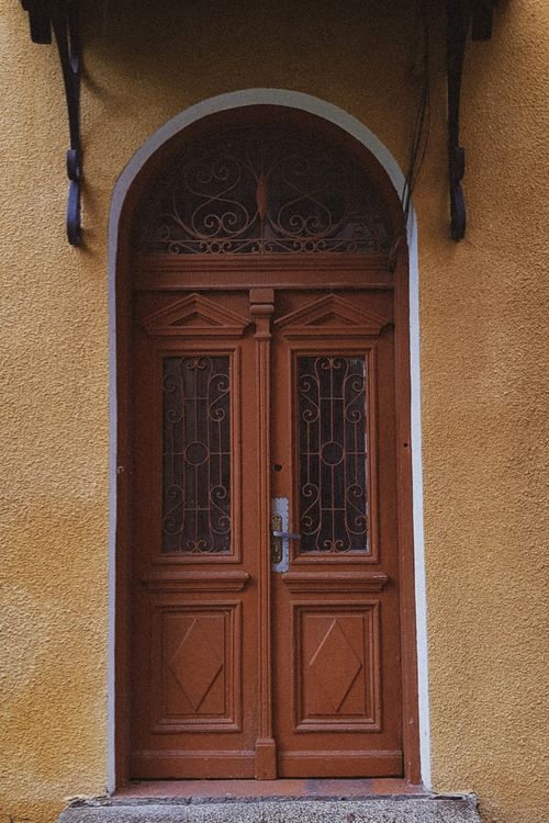 Free A vintage-style wooden door with intricate metalwork set in an arched frame, adding charm to the urban facade. Stock Photo