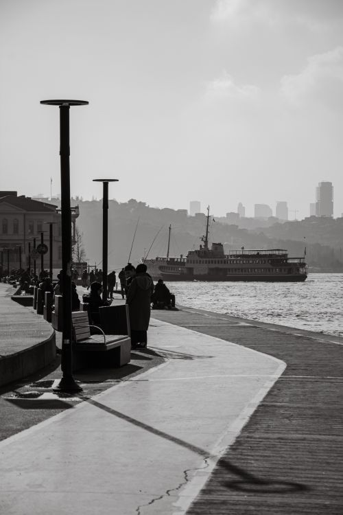 Free A black and white view of a city harbor with a ferry and people on the pier. Stock Photo