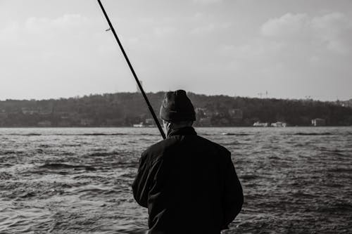 A Grayscale Photo of a Man in Back View Holding a Fishing Rod