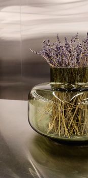 Aesthetic arrangement of dry lavender flowers in a modern glass vase on a reflective surface.