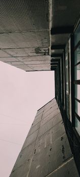 A low angle view of urban architecture with glass windows and concrete surfaces against a white sky.