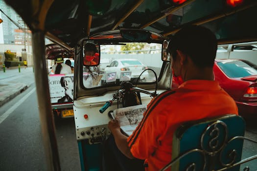 Tuk tuk driver reading a newspaper while navigating through busy Bangkok traffic.