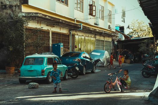 Children play in a vibrant Bangkok street surrounded by colorful cars and buildings, showcasing urban life.