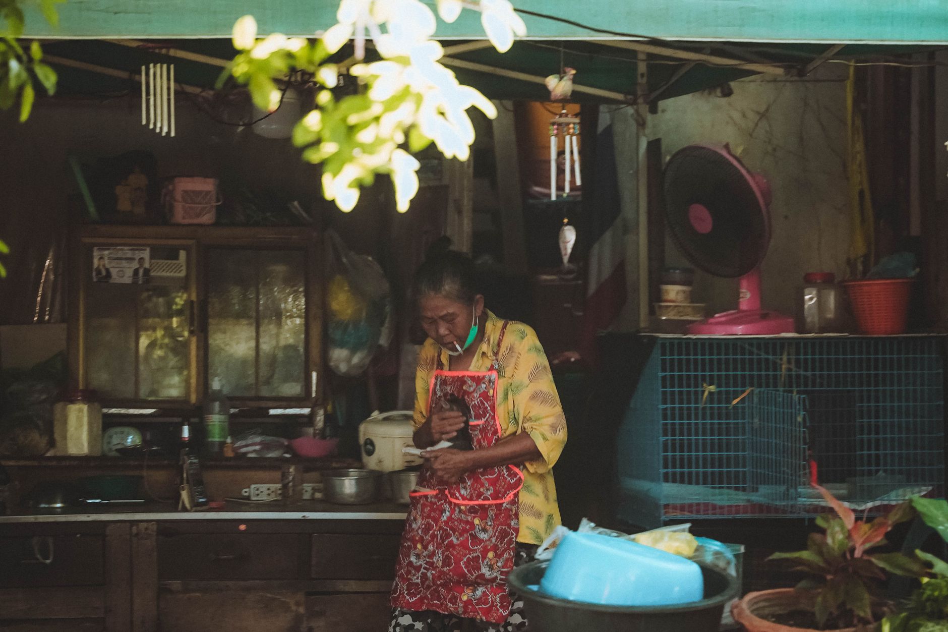 An elderly woman in an apron prepares food at a Bangkok market stall, showcasing Thai street culture.