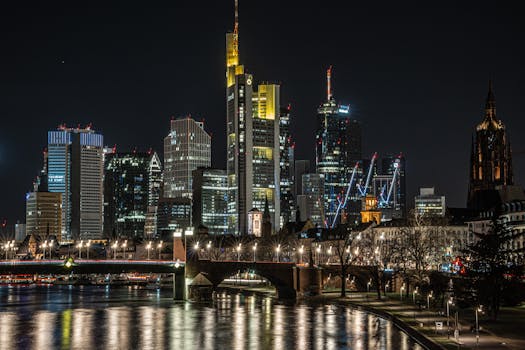 Stunning view of Frankfurt's skyline at night with illuminated skyscrapers reflected in the Main River.