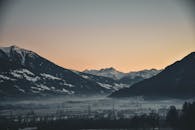 黄昏时分，积雪覆盖的阿尔卑斯山在宁静的冬日景色中，展示出奥地利一个薄雾笼罩的山谷