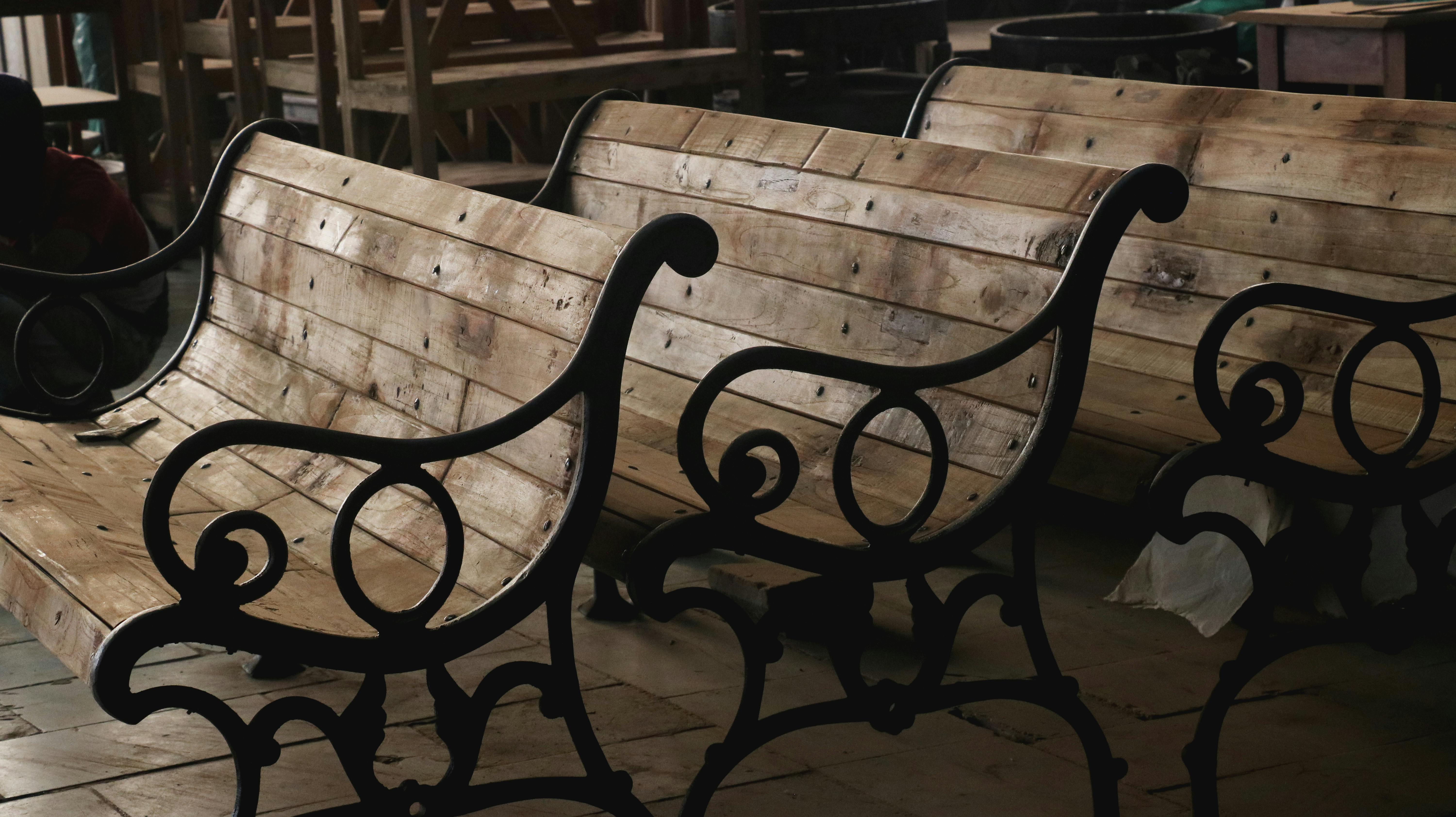 Wooden benches with decorative metal armrests arranged in an indoor workshop setting.