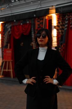 Fashionable woman in black blazer and sunglasses posing outdoors in Almaty, Kazakhstan.