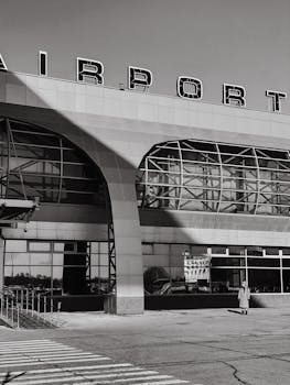 Black and white image of a modern airport exterior with a person standing outside.
