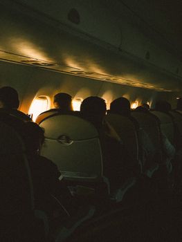Passengers seated inside a dimly lit airplane cabin during flight. Captures the mood of in-flight travel.