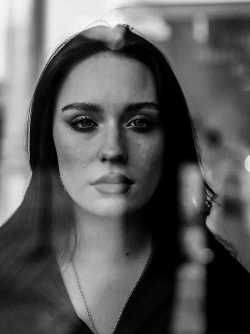 Free Thoughtful black and white portrait of a woman behind glass, expressing depth and emotion. Stock Photo