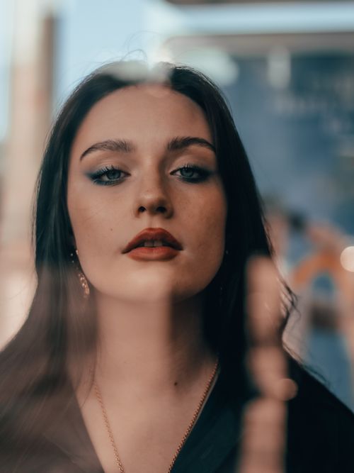 Free Close-up of a woman with striking makeup and red lips, looking through glass with a blurred background. Stock Photo