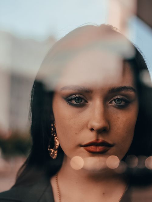 Free Intriguing portrait of a woman with striking blue eyes behind glass, evoking mystery and elegance. Stock Photo