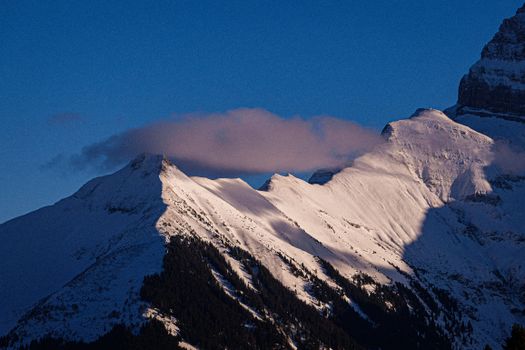 Beautiful snow-covered mountains in Switzerland under a blue sky during twilight, showcasing winter scenery.