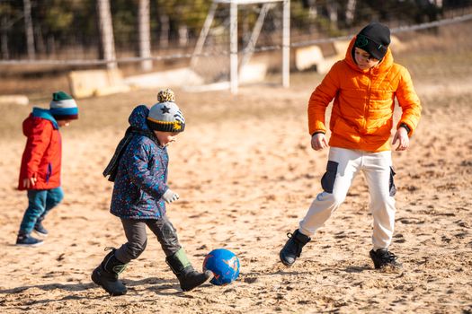 Kids enjoying a soccer game outdoors on a sandy field, dressed in warm winter clothing.