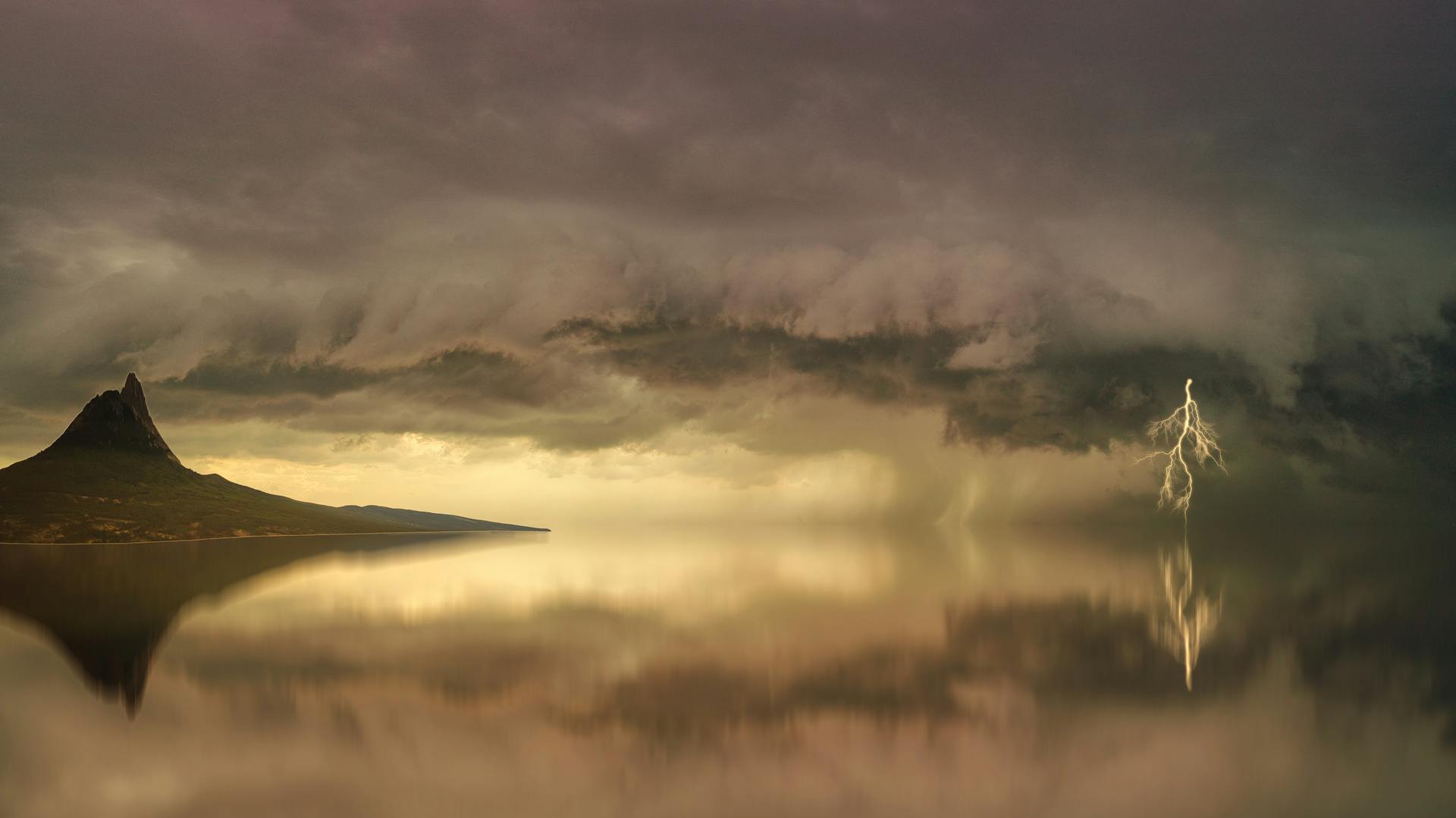 Stunning landscape of a storm over an island with lightning striking the calm water.