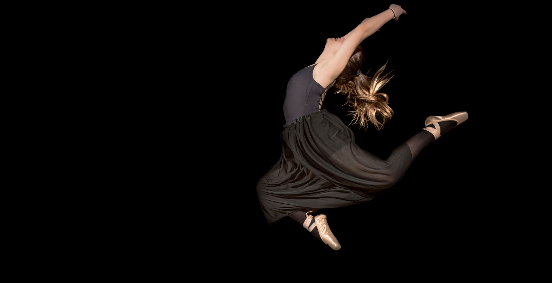 Dynamic capture of a ballerina performing a striking leap against a black backdrop.