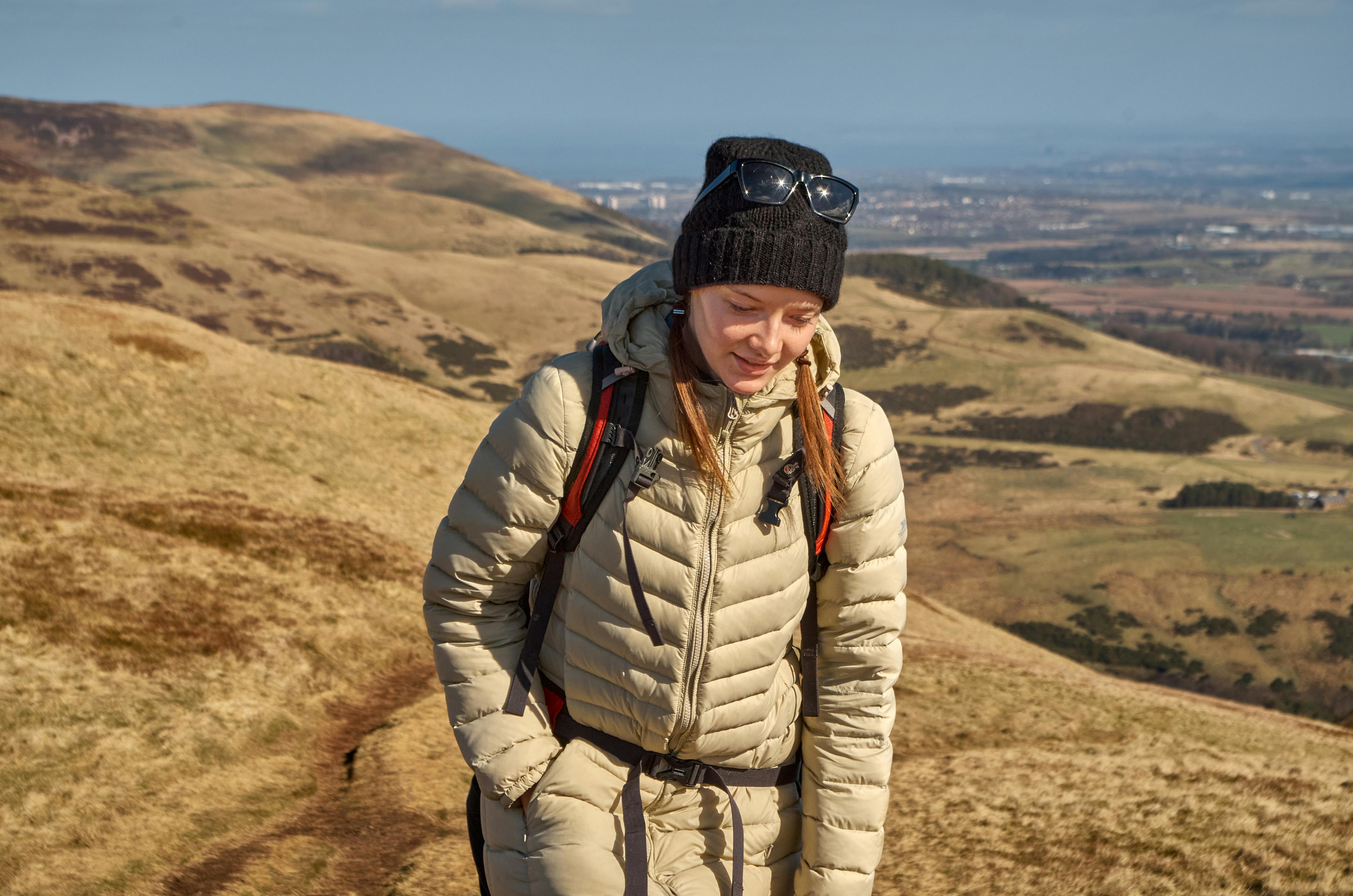 Woman hiking in green hills on a sunny day with a distant city view.