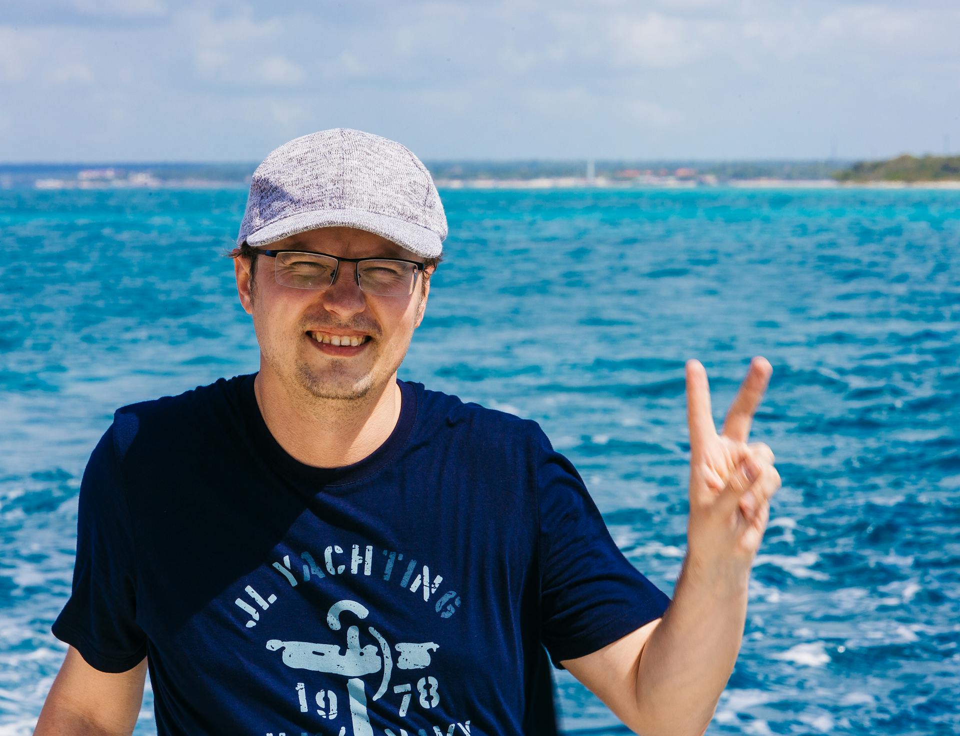 Enjoying a sunny day by the ocean, man poses with a victory sign.
