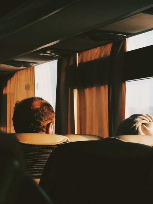 Free Back view of two passengers sitting on a bus, gazing out the window during sunset. Stock Photo