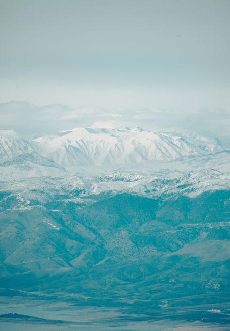 Breathtaking aerial view of snow-covered mountains with a hazy blue sky.