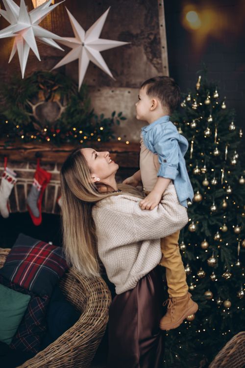 Free Woman holding child near decorated Christmas tree with warm holiday lights indoors. Stock Photo