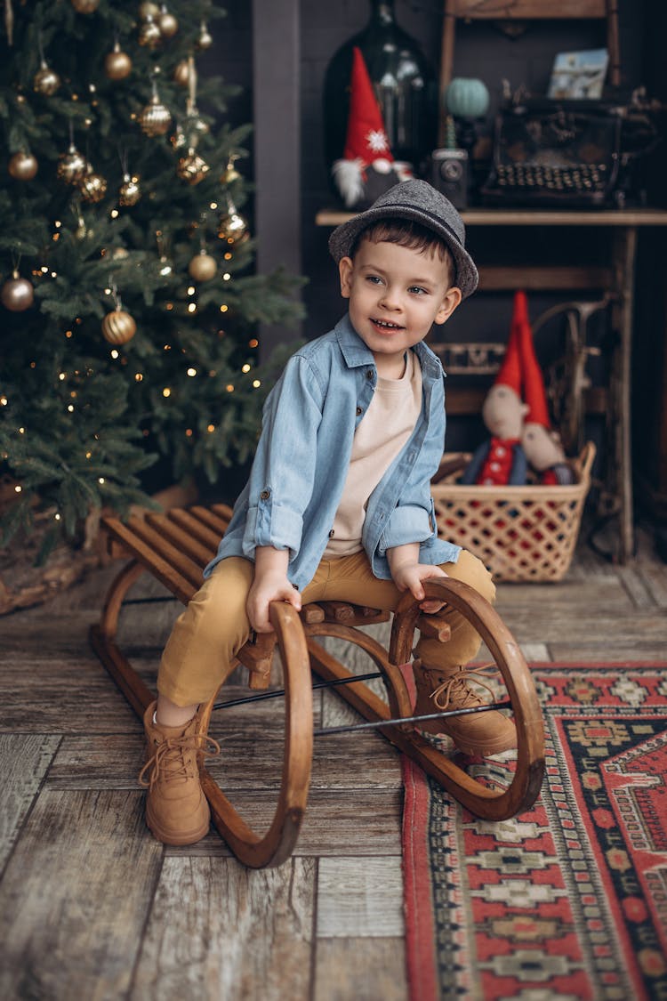 Boy Sitting On Wooden Sled By Christmas Tree