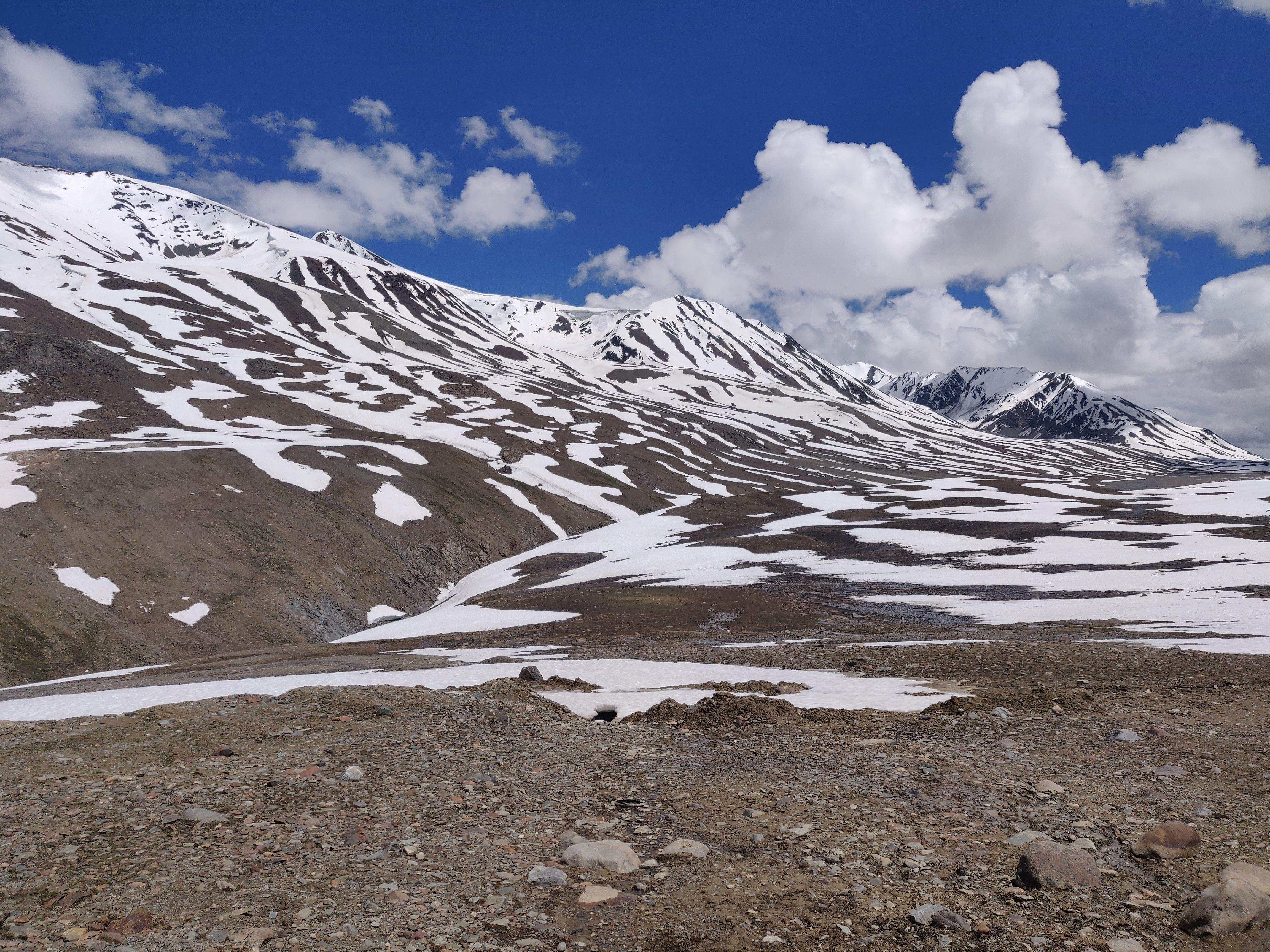 Scenic view of snow-covered mountains with clear blue sky and clouds.