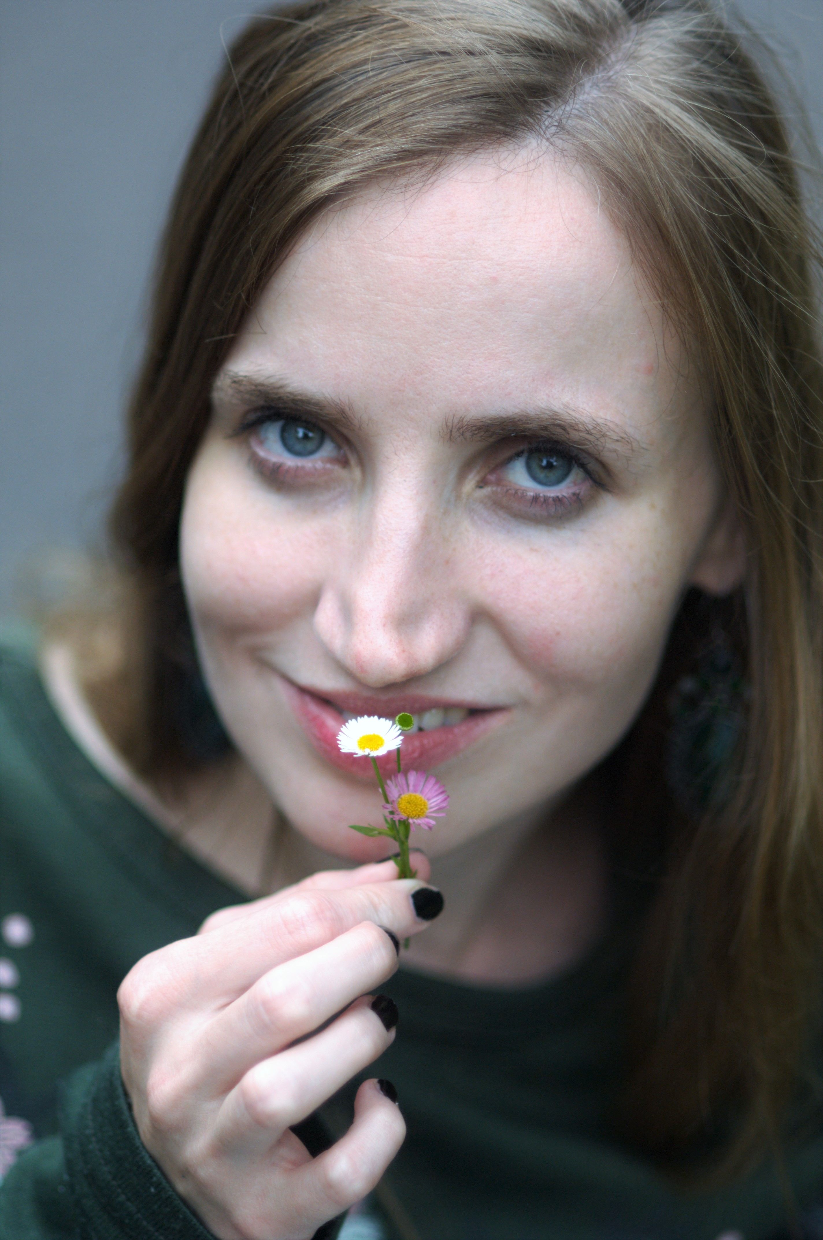 Portrait of a woman smiling and holding a small flower.