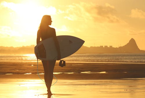 Woman Holding Surf Board Debout Sur Le Rivage Pendant Le Coucher Du Soleil